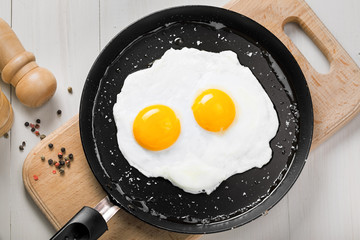 Two fried eggs in a frying pan cooked for breakfast. Delicious international meal on a table. Homemade food, top view.