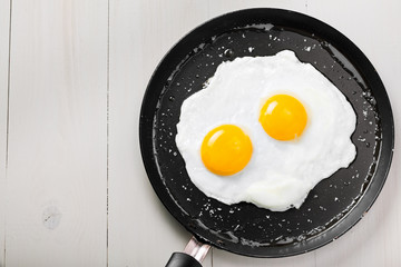 Traditional healthy easy quick breakfast meal made of two fried eggs served on a frying pan. International simple food, top view.