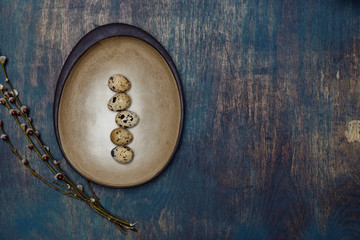 Simple still life with hand-crafted ceramic plate quail eggs and pussy willow on distressed wooden table.