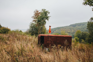 Naklejka premium little girl with a doll stands on the old trailer in the woods