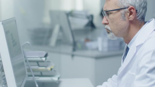 Close-up of Medical Practitioner Typing on a Keyboard Working on His Desktop Computer. In Background His Assistant is Working.  Shot on RED Cinema Camera in 4K (UHD). 