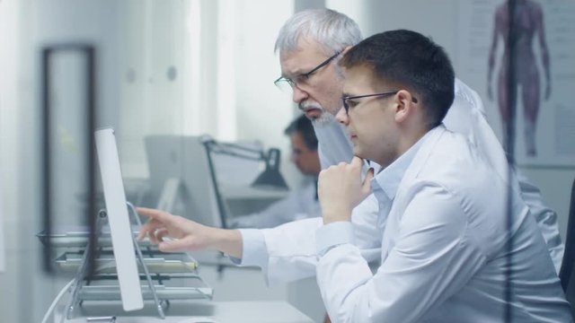 Senior Medical Practitioner and  His Younger Colleague Discuss Medical Matters  Over Personal Computer. Their Office is Bright and Moder Looking. Shot on RED Cinema Camera in 4K (UHD). 