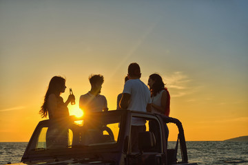 Fototapeta na wymiar Five young people having fun in convertible car at the beach at sunset.