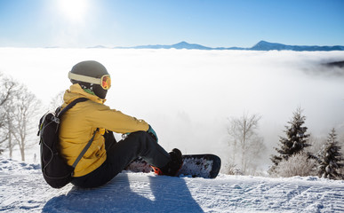 Fototapeta na wymiar Snowboarder sitting and looking at mountain chain in the backgro