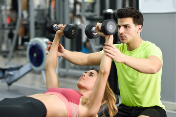 Fototapeta na wymiar Personal trainer helping a young woman lift weights