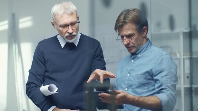 Two Senior Engineers Discussing Technical Details over Tablet Computer. Both Men Look Respectable and Professional. Office is Bright and Modern.  Shot on RED Cinema Camera in 4K (UHD). 