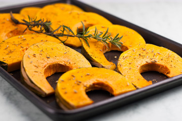 pieces of pumpkin with spices and rosemary branch on the oven tr