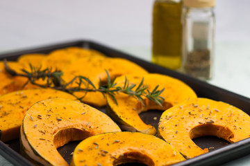 pieces of pumpkin with spices and rosemary branch on the oven tr