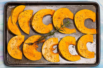 pieces of pumpkin with spices and rosemary branch on the oven tr