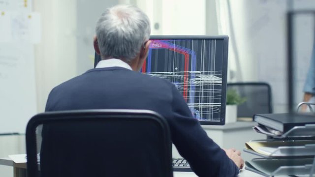 Backview of Senior Architectural Engineer Working with 3D Model on His Personal Computer. Also His Assistant Came in the Office and Took Place at His Desk.  Shot on RED Cinema Camera in 4K (UHD). 