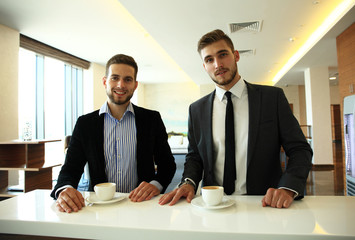 Image of young businessman with cup of coffee communicating with his colleague.