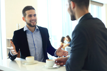 Image of young businessman with cup of coffee communicating with his colleague.