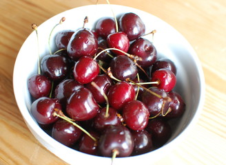 Cherry berries with water drops in the bowl on wood background