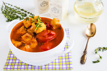 Fish soup with cod, tomato, onion, garlic and thyme in bowl on white table.