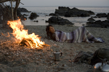femme qui campe en dormant sur la plage au coin du feu à la belle étoile