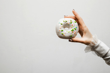 Beautiful female hand holding a white donut against a white wall