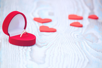 Ring for a marriage proposal and red hearts on wooden table.
