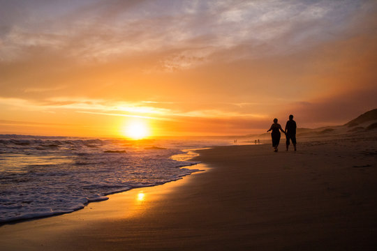 Couples silhouette walking on beach at sunset
