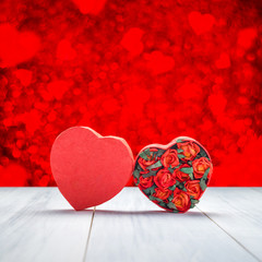 Heart shape box with red roses inside on white wood table top with red bokeh
