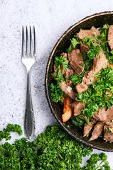Beautiful still life with greenery and meat. Meat, offal, vegetables and parsley leaves lie on a frying pan. Tasty meat dish of European / Asian cuisine. Large sea salt as background.