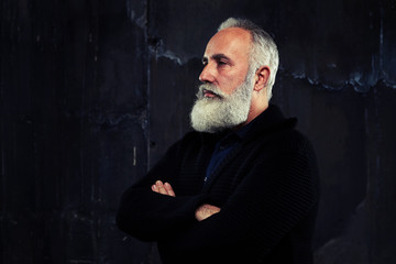A well-built man with grey beard standing and folded arms lookin