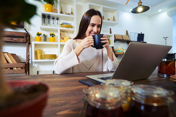 Delighted woman having a cup of tea while looking at the screen