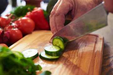 Hands of chef slicing cucumber with a knife on chopping board