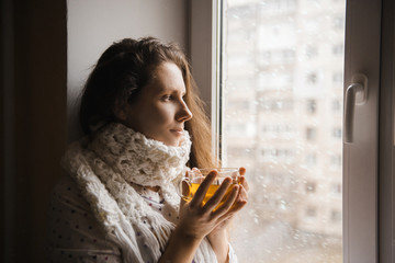 Sick woman with a cup of tea sitting by the window.