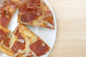 Personal size pepperoni pizza slices on a white plate atop a wood table.