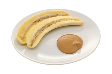 Ripe cut banana and a portion of peanut butter on a plate isolated on a white background.