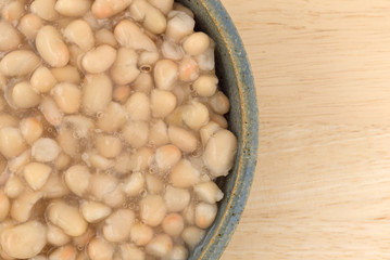 Organic navy beans in a stoneware bowl top close view atop a wood table.