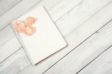 Slices of tangerine (mandarin) with blank notebook on white wooden background