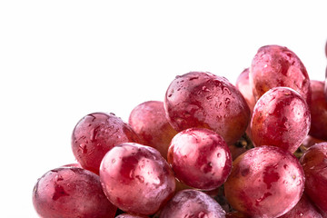 Close up of shiny bundle of purple grapes with water droplets on a white background