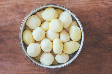 raw peeled potatoes in a round bowl on an old rustic wooden table close-up view from above. tinted photo