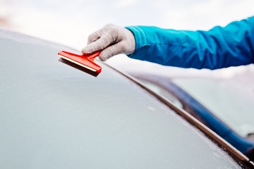 Woman deicing front car windshield with scraper