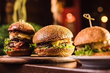 Three juicy tasty burger on the white plate on a dark background
