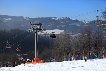 Wyciąg krzesełkowy, narciarze zjeżdżają z góry po śniegu.