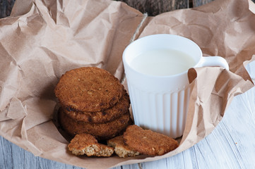 Mug with milk and oatmeal cookies wrapped in paper edge