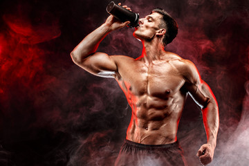 Muscular man with protein drink in shaker over dark smoke background