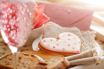 Romantic breakfast in bed. Breakfast tray with heart shaped biscuit, sparkling drink, rose and envelope.