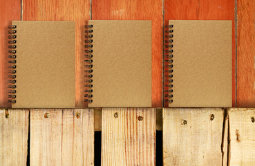 Wooden table with red wood background and blank brown notebook