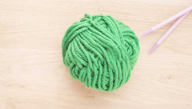 Ball of yarn and knitting needles on wooden table. The needlework thread is green. Concept of traditional hobby and a creative leisure activity.