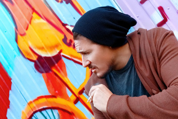 Brutal smokes near colorful wall in the streets of the big city.