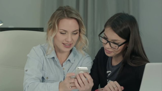 Two smiling coworkers looking at their photos on the phone
