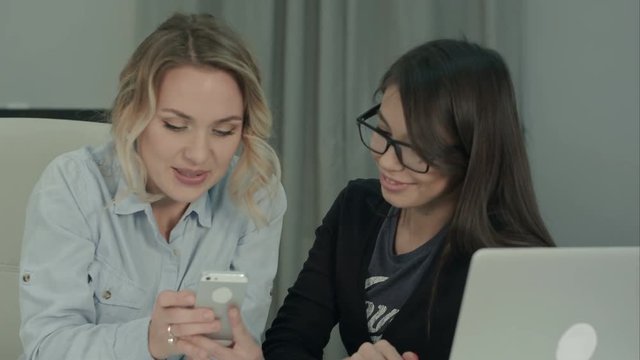 Two office girls laughing and having fun looking at the phone