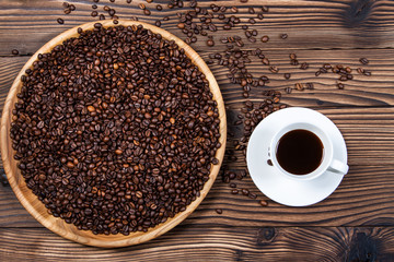 Coffee beans on a large plate and a cup of coffee on a wooden ta