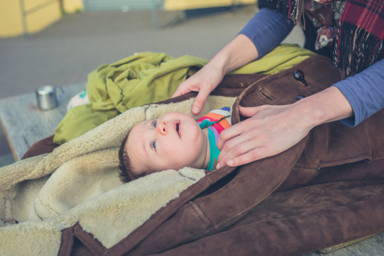 Mother wrapping baby in coat outside