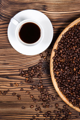 Coffee beans on a large plate and a cup of coffee on a wooden table.