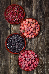 Frozen berries in four bowls on wooden background. Top view.