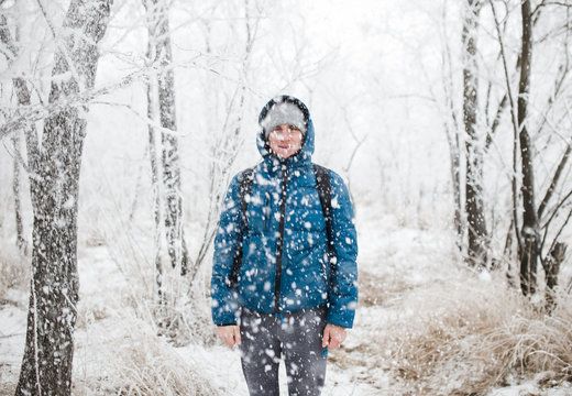Young handsome man standing in snowfall on background of snowy forest.